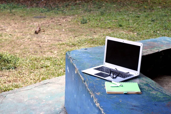 Ordinateur portable, lunettes, cahier et stylo dans un parc extérieur — Photo