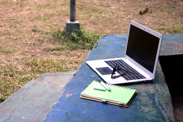 Bordsdator, glasögon, anteckningsbok och penna i en utomhuspark — Stockfoto