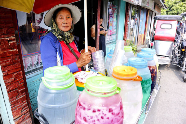 Уличная продавщица продает прохладительные напитки в тележке на тротуаре
