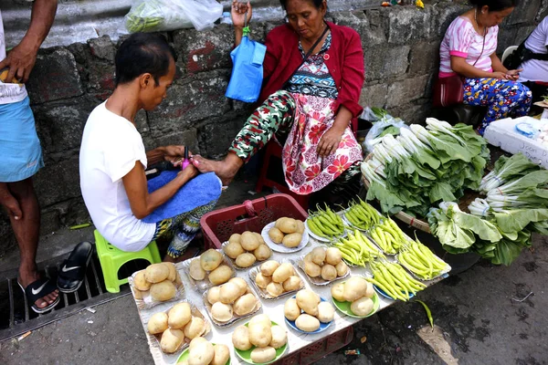 Un vendedor ambulante que vende verduras tiene las uñas limpiadas y pedicuradas mientras espera a un cliente — Foto de Stock