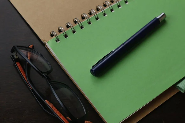 Cuaderno, bolígrafo y anteojos en una mesa — Foto de Stock