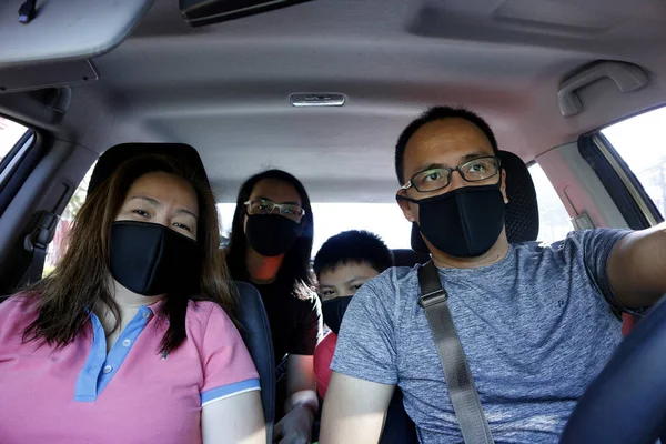 Corona virüsü salgını sırasında arabanın içinde yüz maskesi takan Asyalı bir ailenin fotoğrafı..