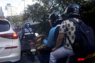 Antipolo City, Philippines - March 13, 2020: Driver of motorcycle taxi and his passenger squeeze through traffic. clipart