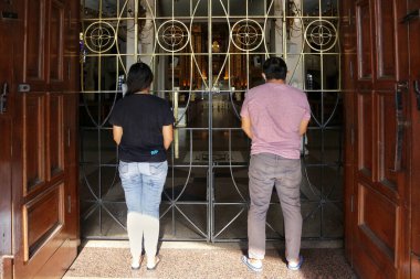 Antipolo City, Philippines - April 4, 2020: People pray outside of the closed and empty Antipolo Cathedral during the lockdown due to the Covid 19 virus outbreak. clipart