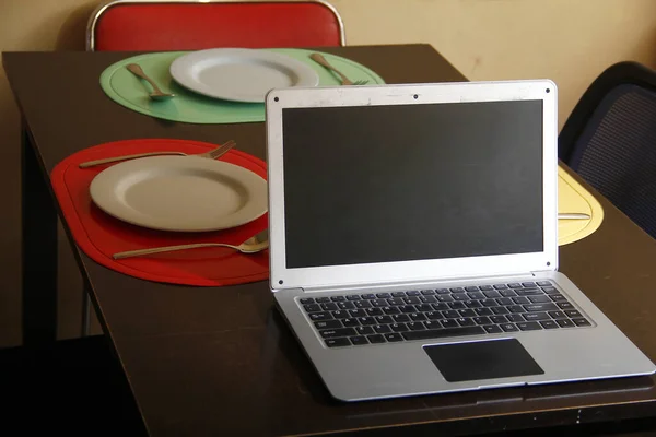 Foto Computadora Portátil Platos Utensilios Una Mesa Comedor — Foto de Stock