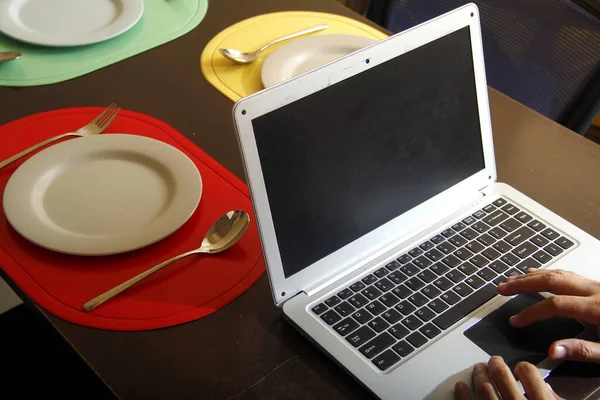 Photo Laptop Computer Hands Typing Plates Utensils Dining Table — Stock Photo, Image