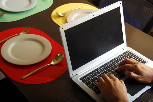 Photo Laptop Computer Hands Typing Plates Utensils Dining Table — Stock Photo, Image