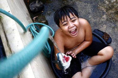 Genç Asyalı bir çocuğun yaz sıcağını yenmek için su hortumuyla su havzasında serinlerken fotoğrafı..