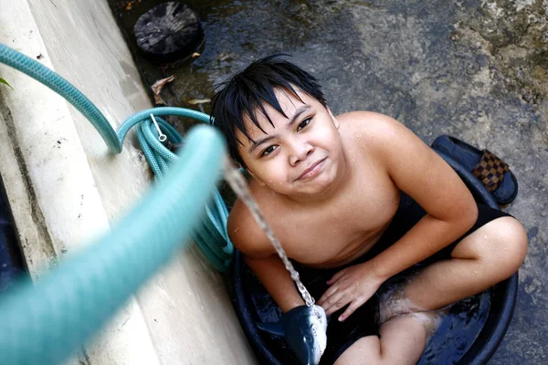 夏の暑さに勝つために仮設のシャワーとして水のホースで水の流域で冷却若いアジアの少年の写真 — ストック写真
