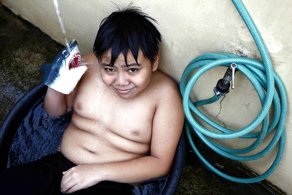 照片中 一个年轻的亚洲男孩在一个水盆里用水管冷却下来 作为一个临时的淋浴 以抵御夏天的炎热 — 图库照片