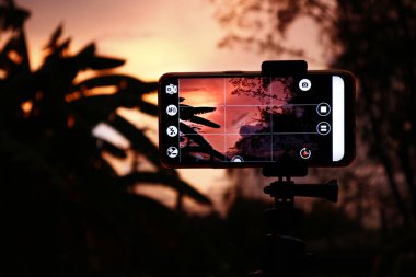 Güzel bir gün batımının fotoğrafını çeken akıllı bir telefonun fotoğrafı.