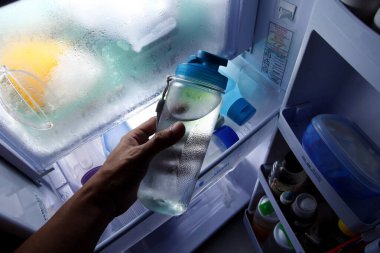 Buzdolabından soğuk suyla dolu plastik bir içecek kadehi alan bir elin fotoğrafı..