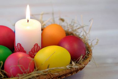 Hasır sepet içinde çok renkli Paskalya yumurtaları ve yanan bir muma yalan. Yakın çekim görünümü.