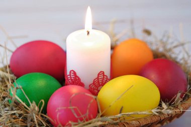 Hasır sepet içinde Paskalya yumurtaları ve yanan bir muma yalan. Yakın çekim görünümü.