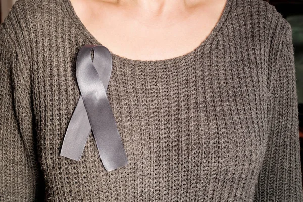 A gray ribbon of awareness of Parkinson\'s disease is attached to the female breast. As a symbol of the Day of Parkinson.