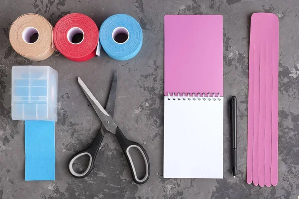 Rollos de cinta de kinesiología para atletas, tijeras y cuaderno con pluma sobre fondo blanco, vista superior . — Foto de Stock