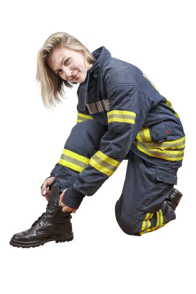 Joven bombera de belleza en un traje protector atando cordones en botas y sonriendo —  Fotos de Stock