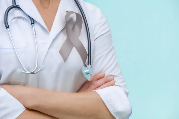 Doctor with folded arms and a stethoscope on his neck, shows a grey ribbon close-up on uniform