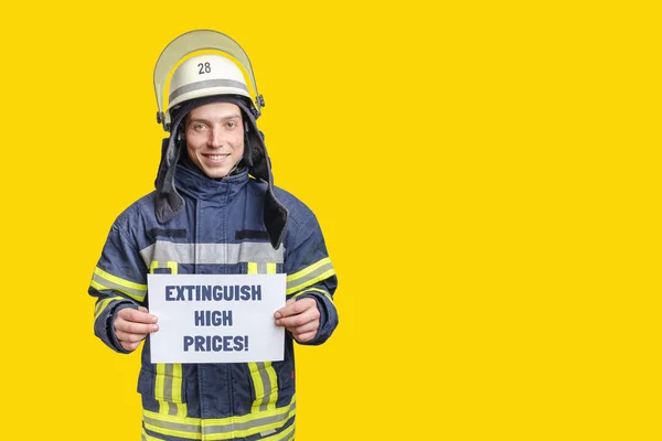 Mladý usměvavý hasič v uniformě a helmě dívá do kamery a drží papírový list — Stock fotografie