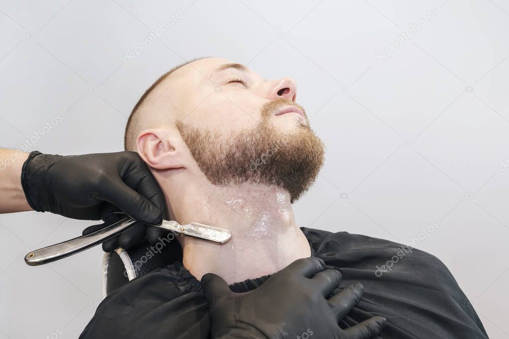 Barbers hand with a razor shaves a beard on the patients throat.