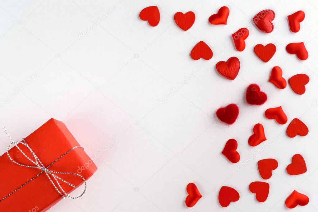 Festive composition from tied red gift box, snowflakes and hearts scattered on white background, valentines day concept