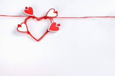 Kalp şeklinde kırmızı bir iple sarılmış. Beyaz bir zemin üzerinde kalp şeklinde mandallar var..