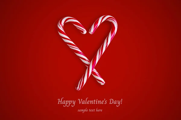 Two red and white candy canes in the shape of heart on a red background. — Stock Photo, Image