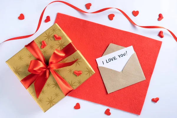 Arany ajándék doboz piros szalaggal a szöveten, boríték, kártya leírással Szeretlek és kis szívek — Stock Fotó