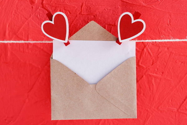 пустой лист бумаги в конверте висит на веревке, прикрепленной к сердечной прищепке на красном фоне
.