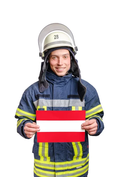 Young smiling firefighter looking to the camera and holding paper sheet with austrian flag — Stok fotoğraf