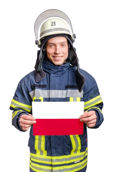 Junger lächelnder Feuerwehrmann blickt in die Kamera und hält Papierbogen mit polnischer Fahne in der Hand — Stockfoto