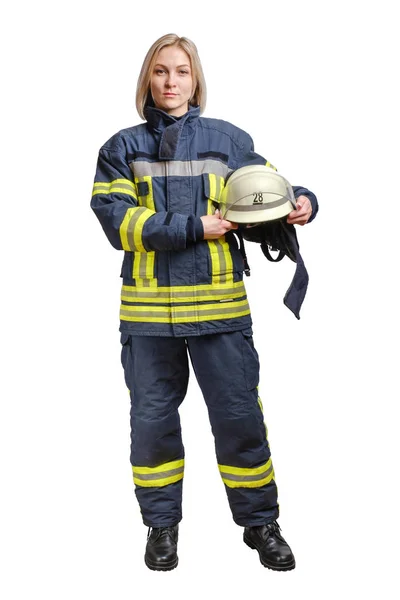 A young brave girl firefighter in a fireproof uniform stands and looks at the camera with a helmet in her hands. — Stock Photo, Image