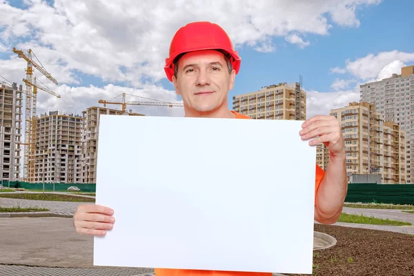 Portret uśmiechnięty przystojny pracownik w średnim wieku w czerwonym, twardym kapeluszu, patrzący w kamerę i trzymający pusty papier — Zdjęcie stockowe