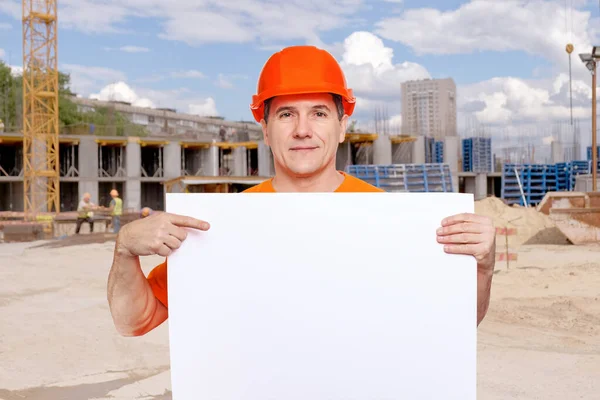 Portret uśmiechnięty przystojny pracownik w średnim wieku noszący pomarańczowy, twardy kapelusz, patrzący w kamerę i trzymający puste prześcieradło — Zdjęcie stockowe