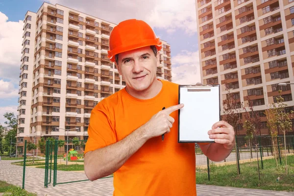 Portret uśmiechnięty przystojny pracownik w średnim wieku noszący pomarańczowy, twardy kapelusz, patrzący w kamerę i trzymający schowek — Zdjęcie stockowe