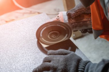 tiler cuts a square hole in the tile using an angle grinder.