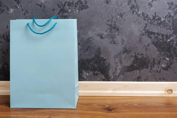 木制地板上的蓝纸购物袋与混凝土墙背衬在一起. — 图库照片