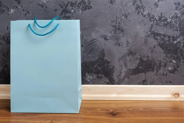 Borsa shopping di carta blu sul pavimento di legno su uno sfondo muro di cemento . — Foto Stock