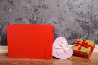 kırmızı kağıt çanta ve iki hediye kutusu tahta zeminde beton duvara karşı yatıyordu.