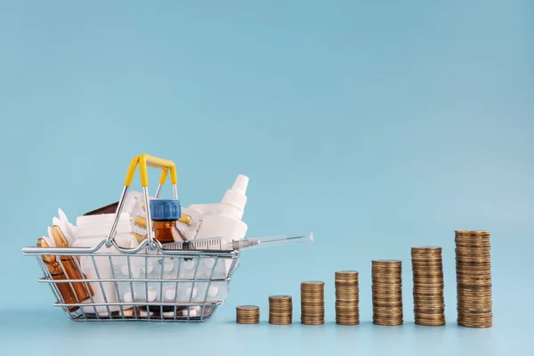Shopping basket filled medicinal tablets, stacks of coins in a row ascending on blue background. — Stock Photo, Image
