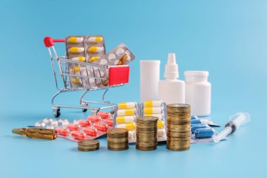 Ardı ardına yükselen bozuk paralar, alışveriş arabaları ilaç tabletleri ve haplarla dolu, arka planda seçici bir odak noktası var. en pahalı uyuşturucular veya yükselen uyuşturucu fiyatları kavramı.