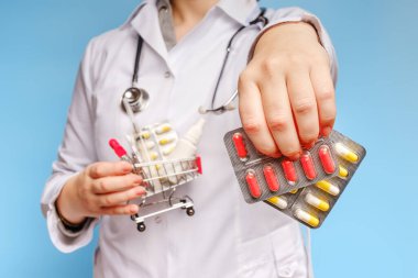 Doktorlardan biri hapları yakın çekimde tutuyor, diğeri de ilaç, şırınga ve ilaç dolu bir alışveriş arabası tutuyor.