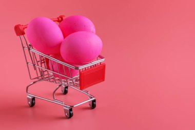 Pembe arka planda Paskalya yumurtası olan bir alışveriş arabası. Paskalya alışverişi ve satış, kopyalama alanı