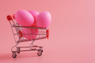 Pembe arka planda Paskalya yumurtası olan bir alışveriş arabası. Bayramlık Paskalya alışverişi ve satışı, kopyalama alanı