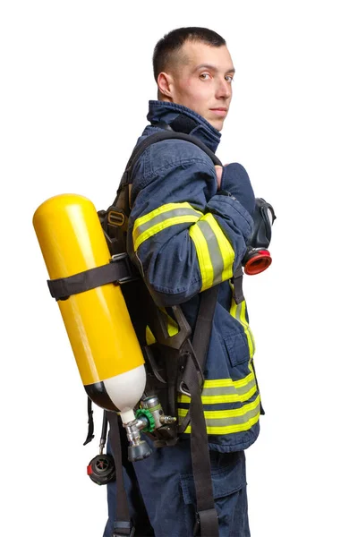 青い背景に隔離された耐火制服で彼の背中に完全な顔の呼吸器と呼吸空気シリンダーアセンブリとプロファイルでポーズ若い白人消防士 — ストック写真