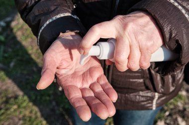 Dezenfektan şişesine sıklıkla el temizleme ve Coronavirus Covid-19 ve diğer mikropları, bakterileri ve virüsleri önlemek için alkol antiseptik jeli kullanan 74 yaşındaki yaşlı bir kadın. Yakın görünüm