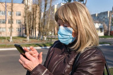 Kafkasyalı yaşlı kadın Coronavirus salgınını korumak için maske takıyor ve ailesi ve arkadaşlarıyla konuşmak için akıllı telefon kullanıyor..