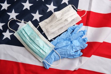 Amerikan bayrağı arka planında cerrahi koruyucu maskeler ve eldivenler kullanılmış. Covid-19 karantinası. Düz yatış, üst görünüm