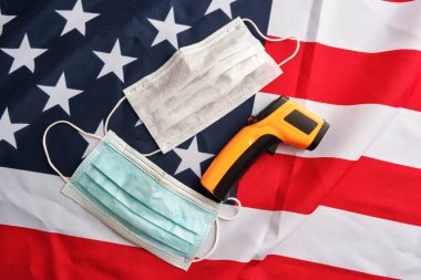Amerikan bayrağı arka planında koruyucu maskeler ve temas olmayan kızılötesi termometre kullanılmış. Covid-19 karantinası. Düz yatış, üst görünüm
