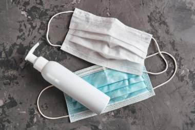 İki kullanılmış koruyucu maske ve dezenfektan şişesi alkol jeli. Gri beton arka plana yakın. Covid-19 karantinası. Düz yatış, üst görünüm